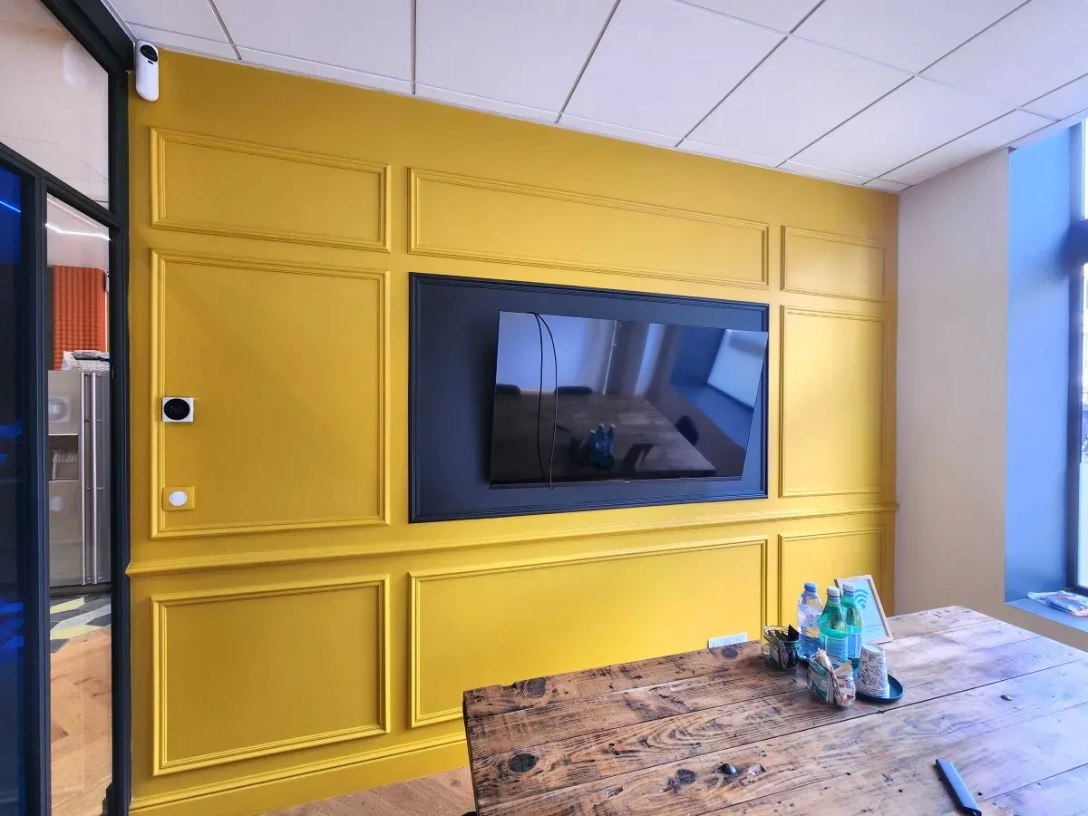Mur jaune à moulures avec téléviseur encastré, dans le showroom Direct Décor
